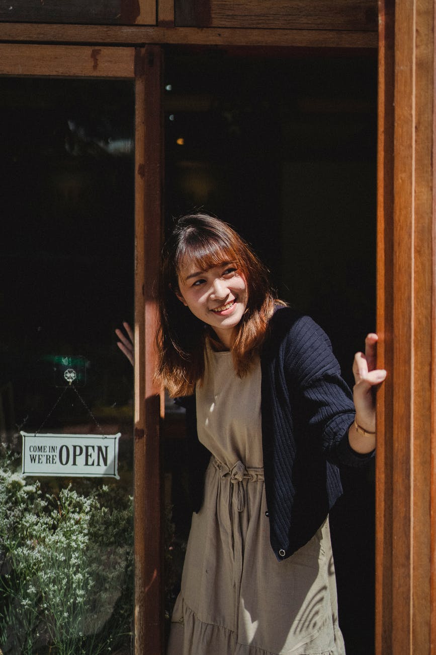 smiling asian woman in apron opening store door