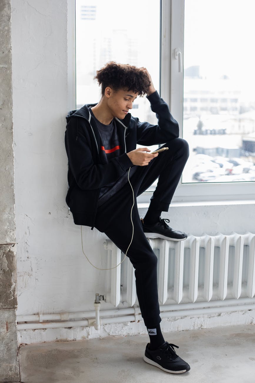 black man sitting on windowsill and using smartphone