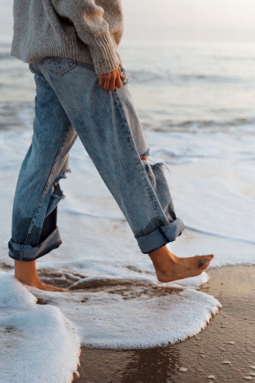 anonymous barefooted woman strolling on wet sandy seashore