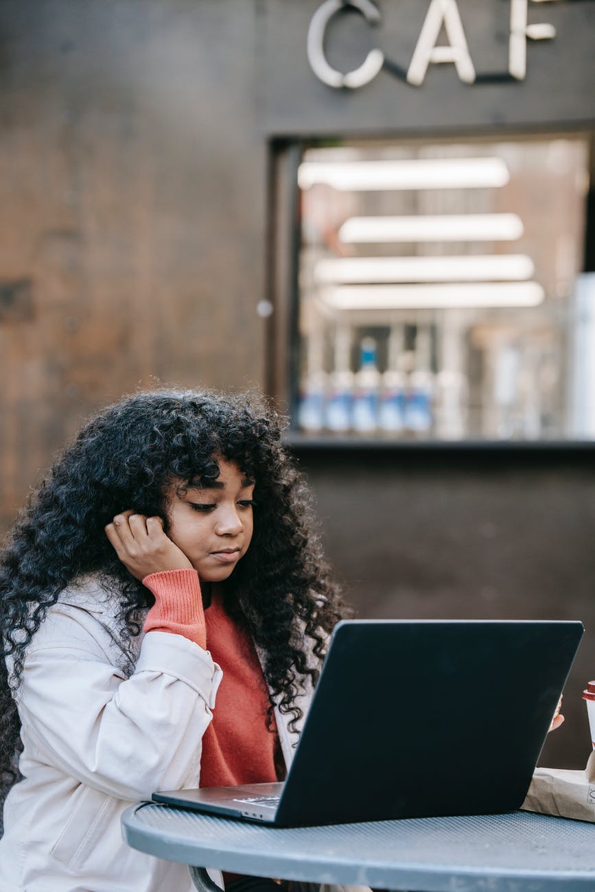 thoughtful black woman working on laptop in street cafeteria