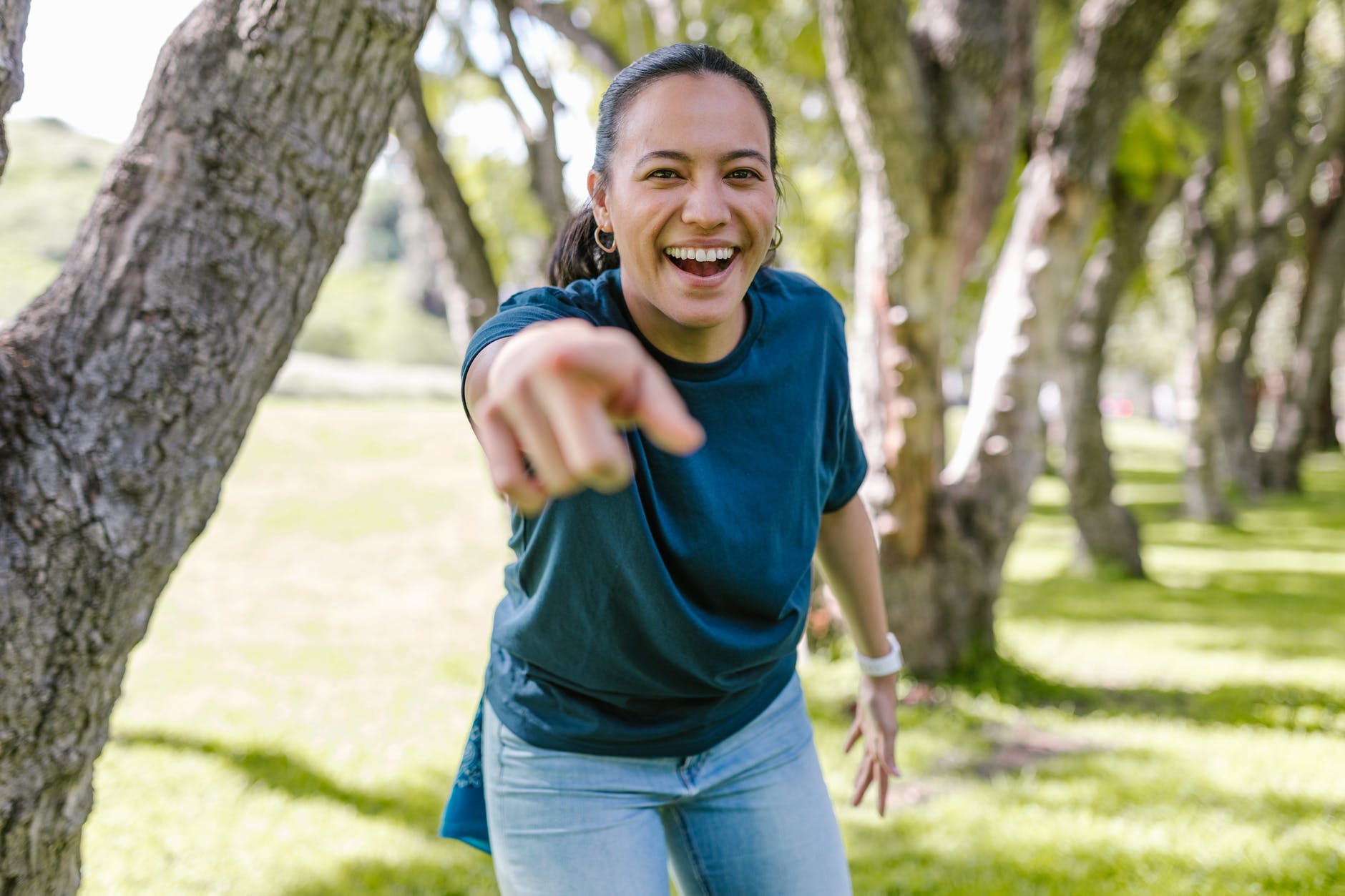 smiling woman in green crew neck t shirt and blue denim jeans standing beside brown tree