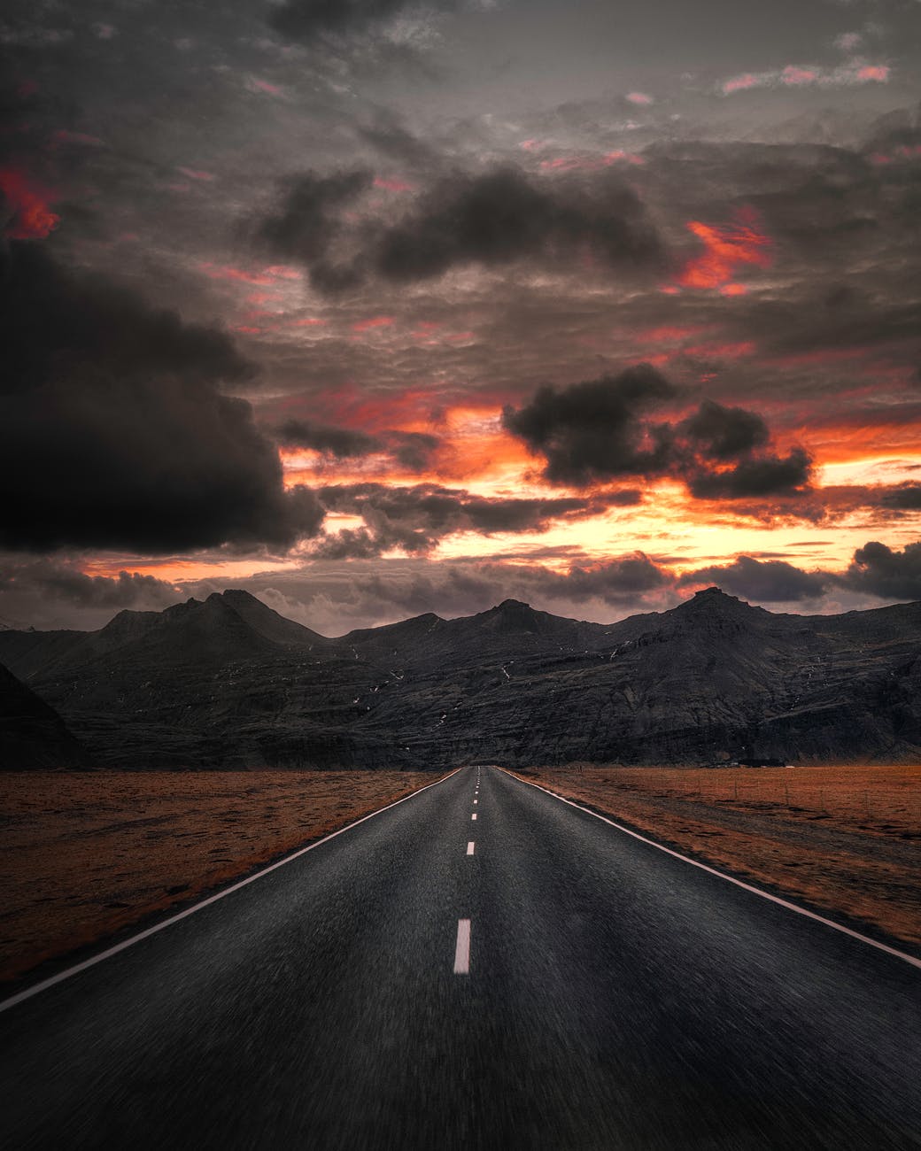 black asphalt road near mountains under cloudy sky