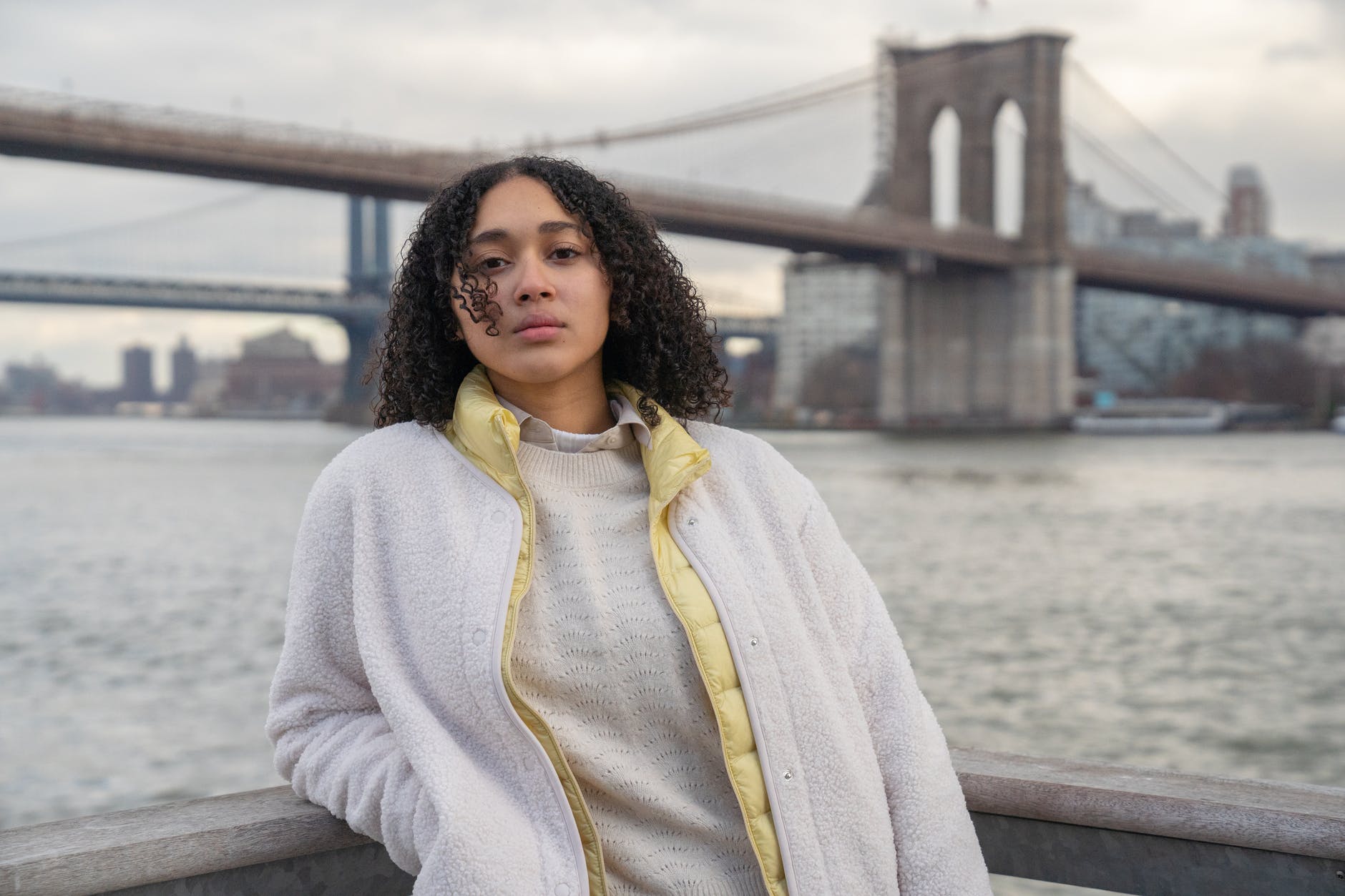 thoughtful hispanic lady standing near river and bridge in city