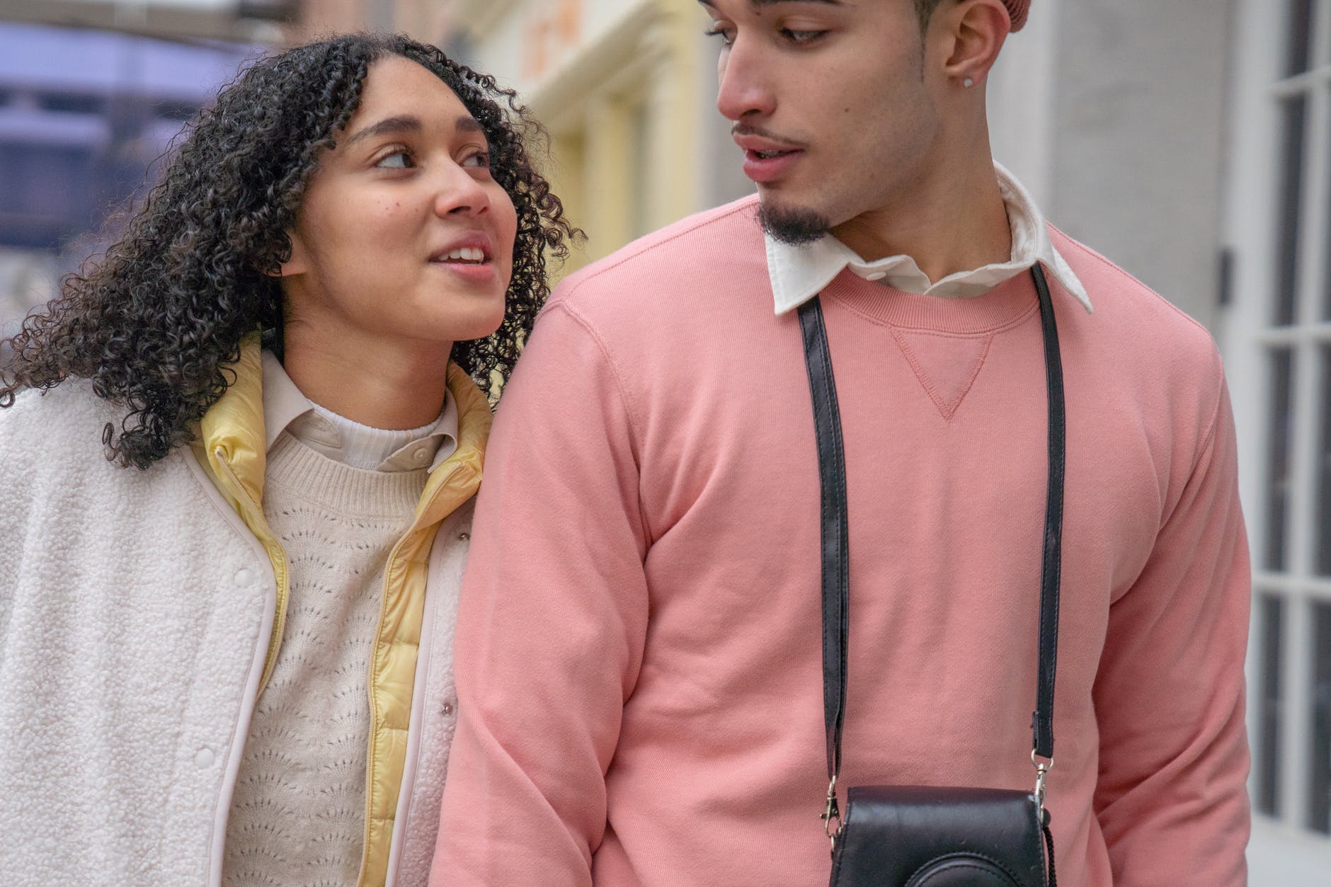 positive young hispanic couple looking at each other while strolling in city