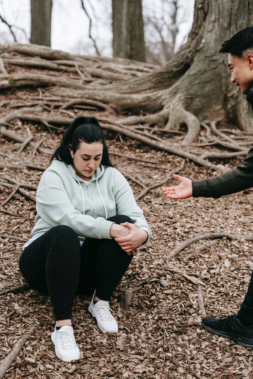 crop ethnic man giving hand to upset woman in autumn forest